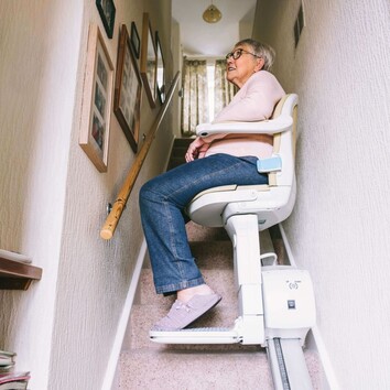 505200910 | © okrasiuk - stock.adobe.com Eine Frau fährt auf einem Sitzlift eine enge, gerade Treppe nach oben