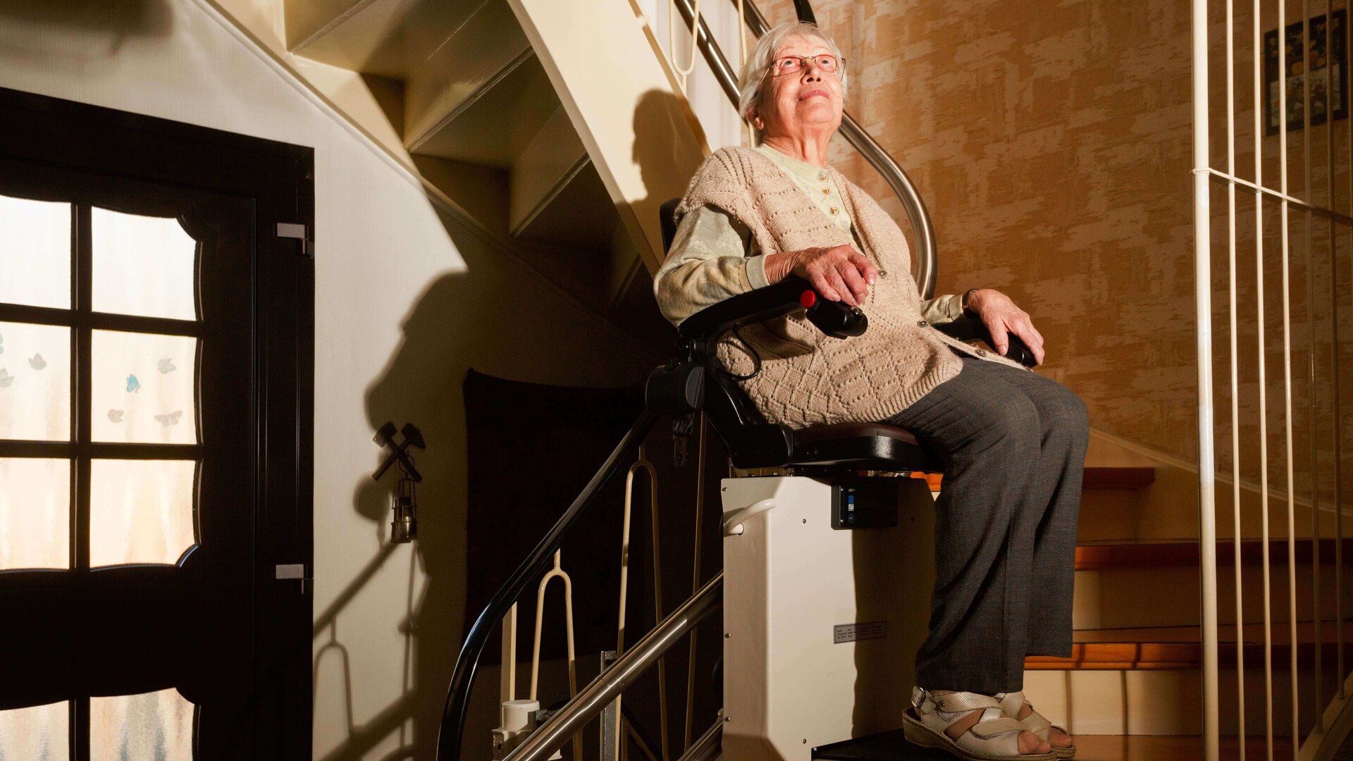 Eine Seniorin fährt auf einem Sitzlift die Treppe hinauf