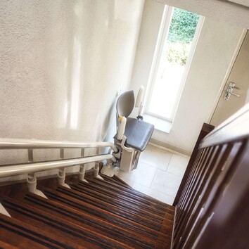 355639237 | © annebel146 - stock.adobe.com Ein Sitzlift parkt am unteren Ende einer Treppe