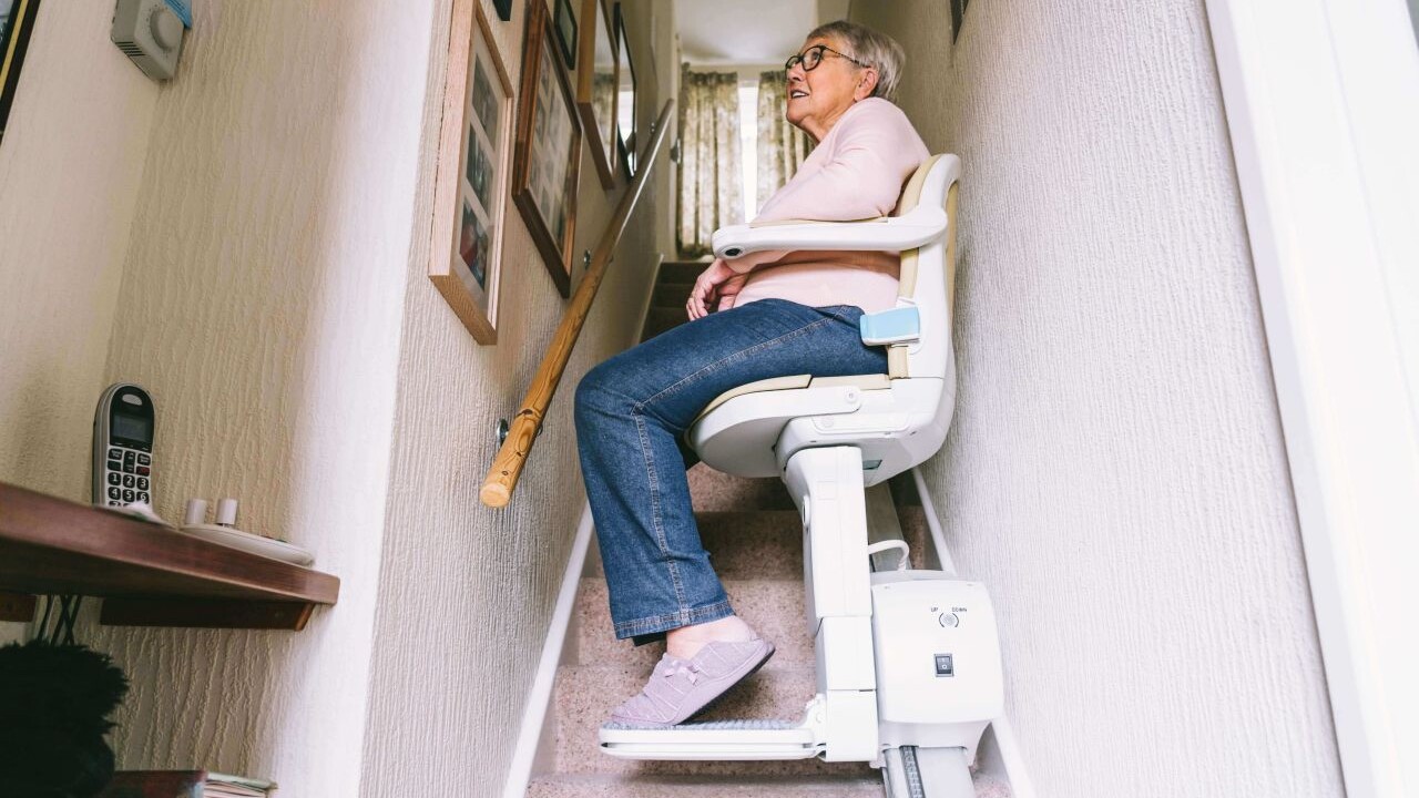 Eine Frau fährt auf einem Sitzlift eine enge, gerade Treppe nach oben