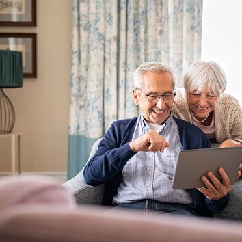 442916239 | © Rido - stock.adobe.com Lächelndes Seniorenpaar schaut zusammen auf ein Tablet