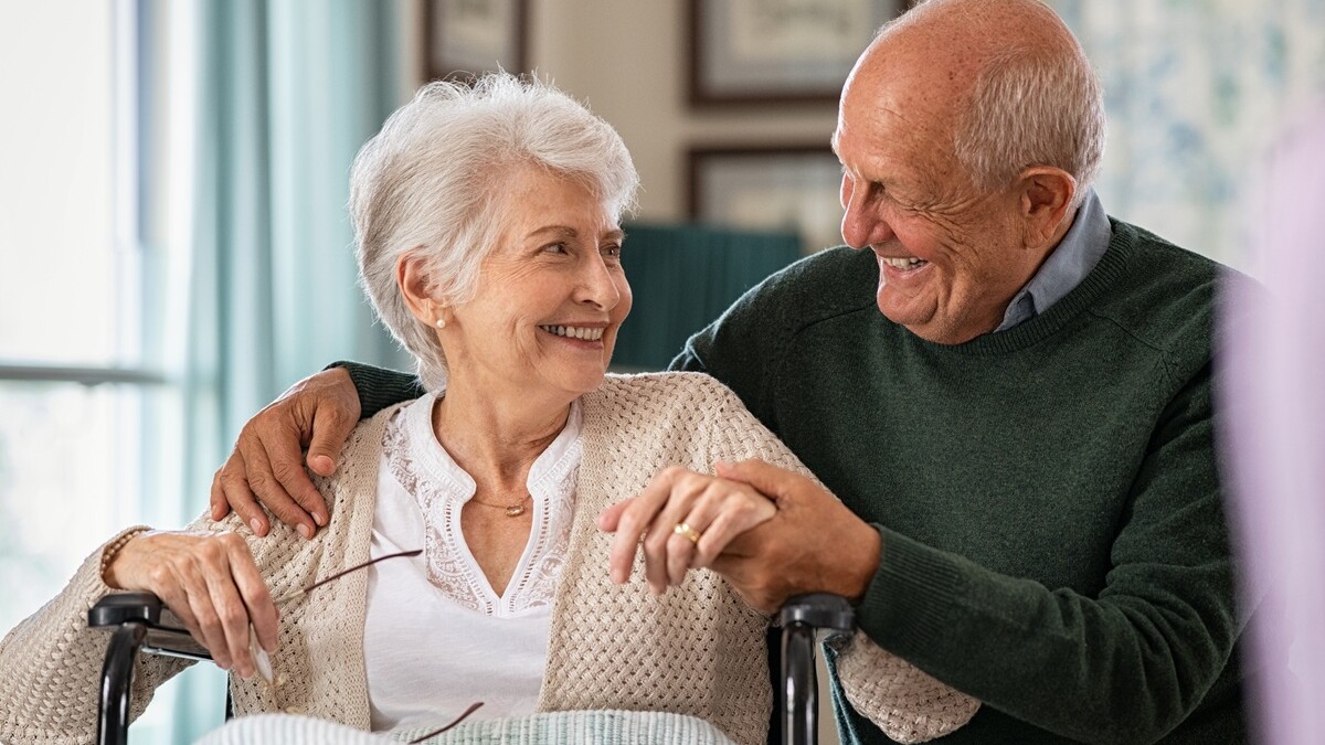 435778564 | © Rido - stock.adobe.com Seniorin im Rollstuhl und ein Senior daneben schauen und lächeln sich an