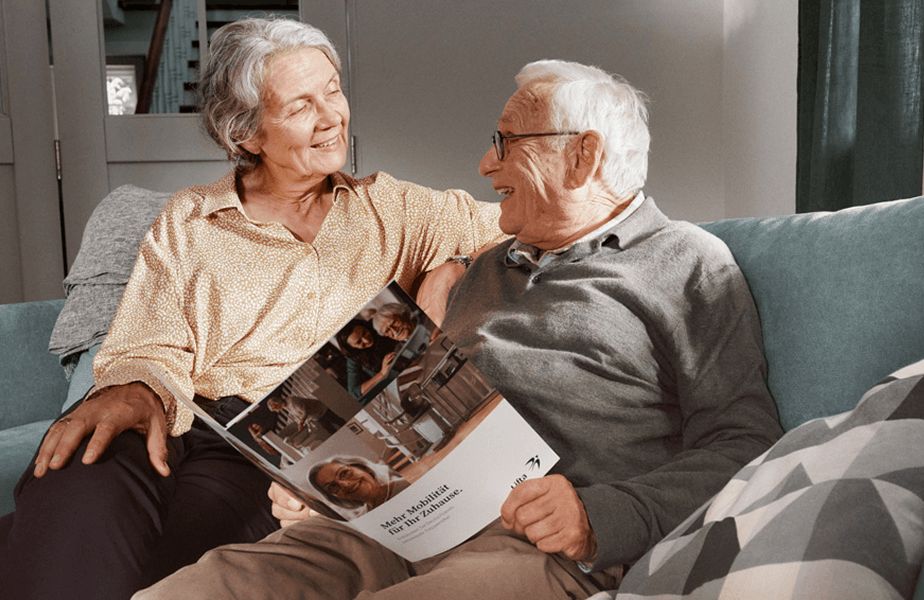 Ältere Dame und Herr sitzen mit einer Lifta Broschüre auf dem Sofa